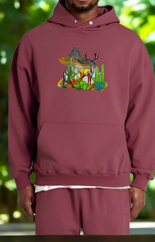 Embroidered hoodie featuring a mountain deer with antlers, surrounded by snow-dusted peaks and desert cacti, in a blend of earthy and glacial colors.