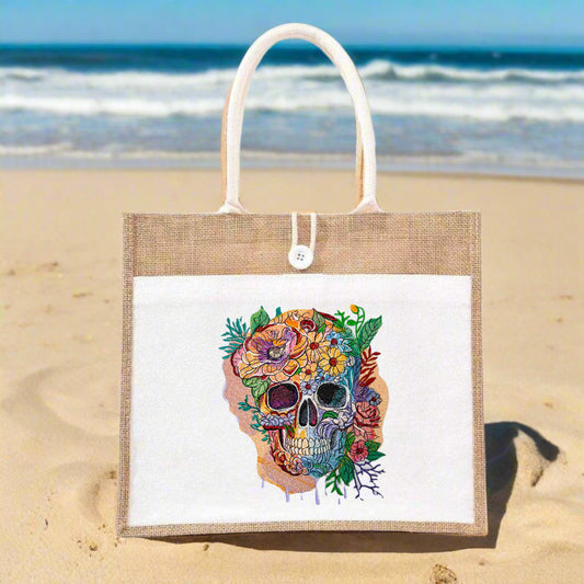 A tote bag featuring a skull embroidered with colorful floral patterns and gold accents on a beige background.