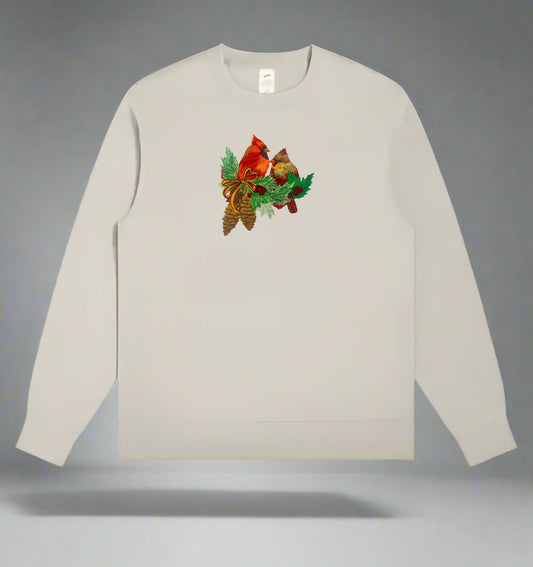 Light beige crewneck sweatshirt with embroidered pair of cardinals framed by pine foliage, holly, pinecones, and a decorative bow.