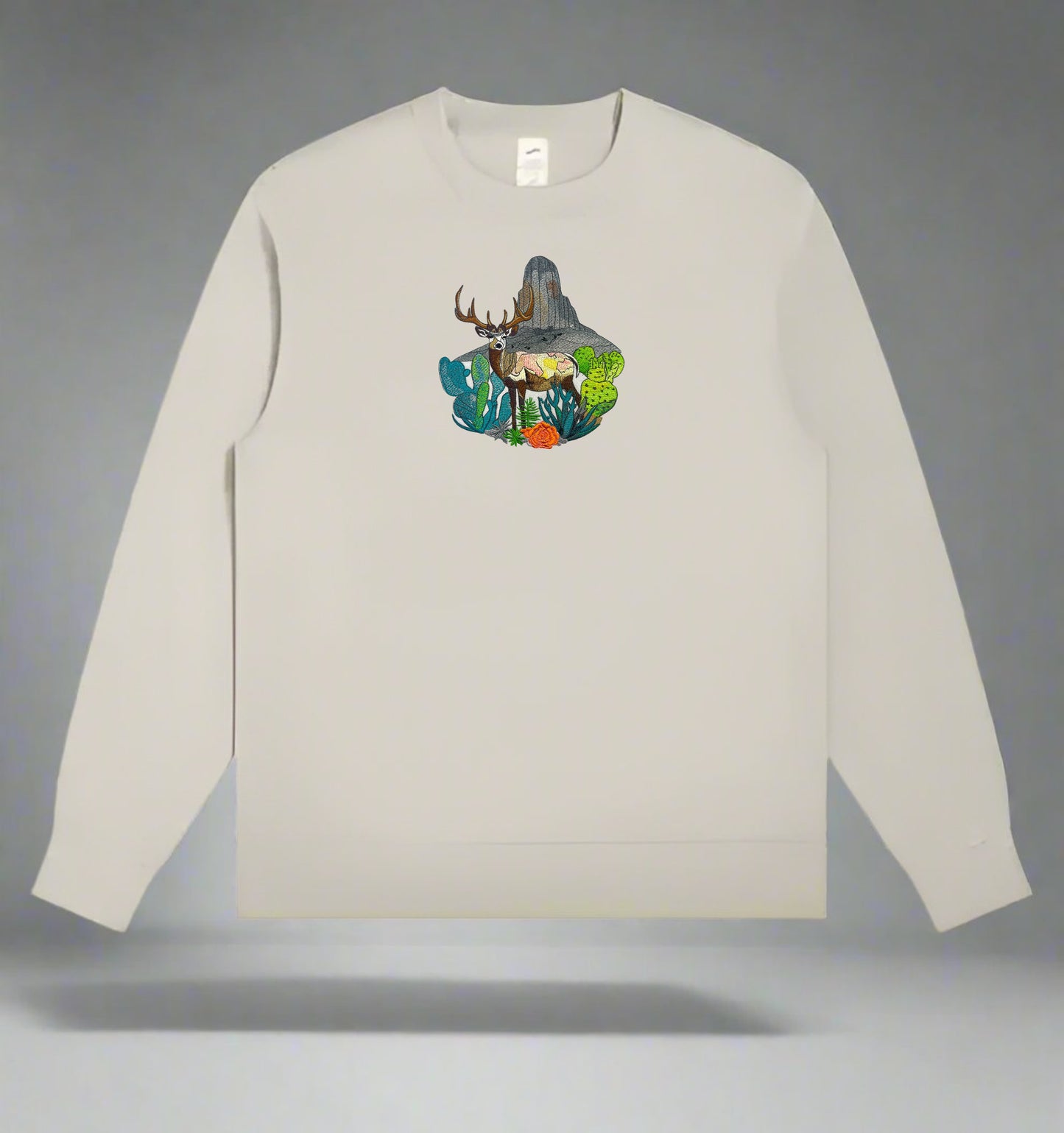 Embroidered crewneck sweatshirt with a design of a mountain deer surrounded by wildflowers and alpine pines against a rainbow-colored background.