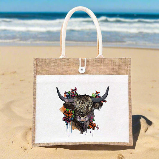 A tote bag with an embroidered image of a Highland cow with heather and wildflowers on its head.