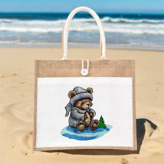 Embroidery of a bear wearing a scarf and hat, sitting on a snowy surface with a crescent moon and a small tree in the background.