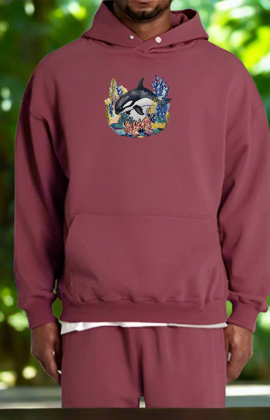 Maroon hoodie with a whale design worn by a person against a blurred green background