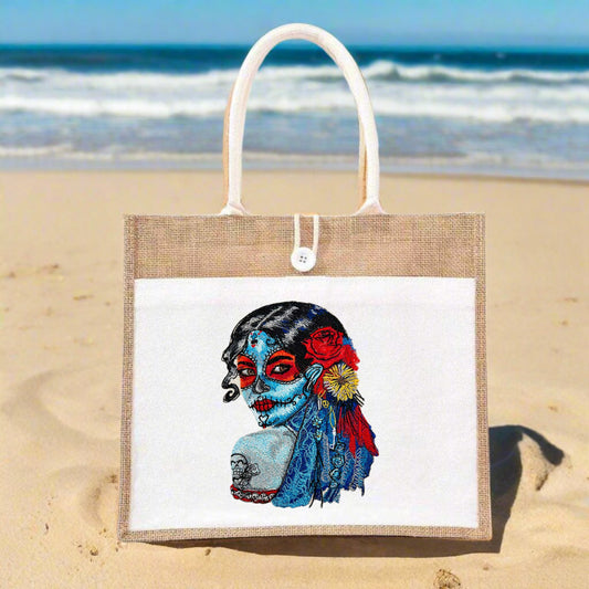 A tote handbag made of jute featuring detailed embroidery of a character with a skull face, floral patterns, and tribal geometric designs.