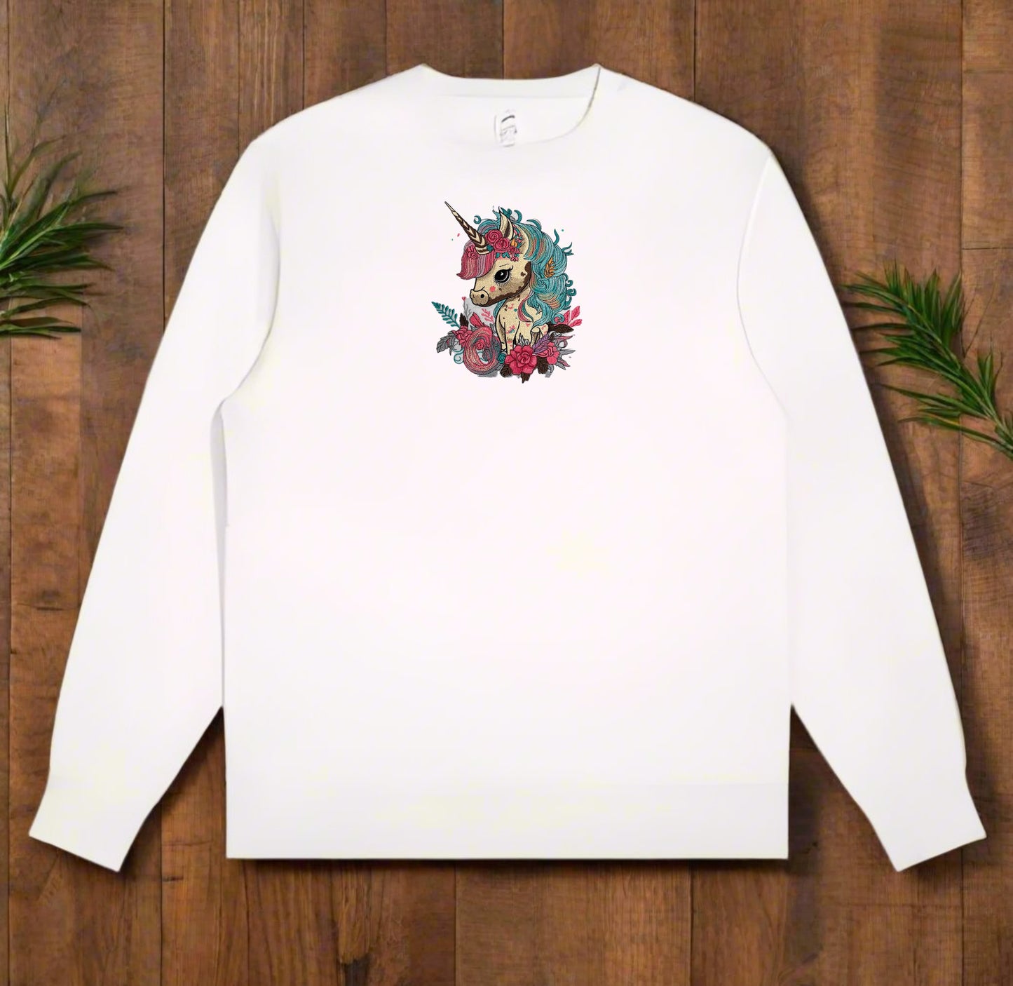 White long-sleeve sweatshirt with a colorful unicorn design on a wooden surface.