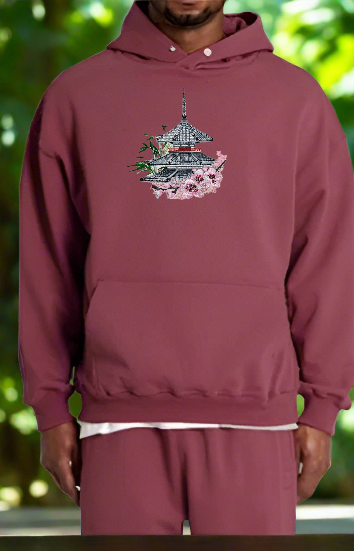 Maroon hoodie with a pagoda design on a blurred green background