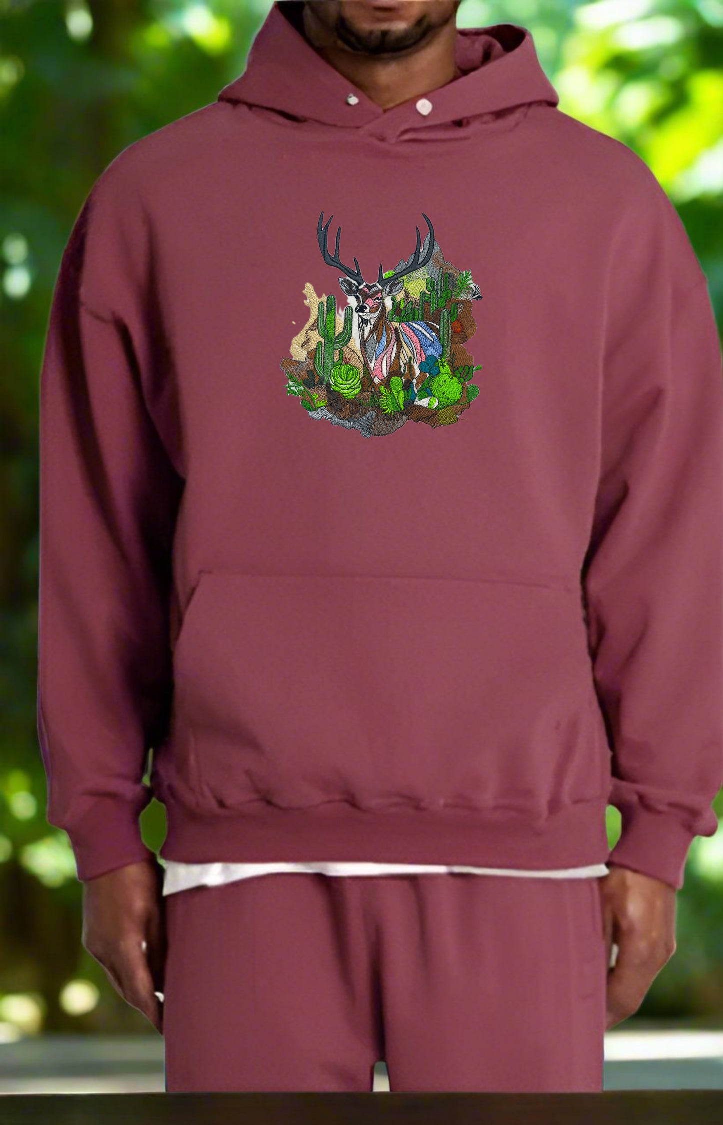 Embroidered hoodie featuring a mountain deer with Ombre antlers, surrounded by wildflowers and alpine pines, in a colorful design.