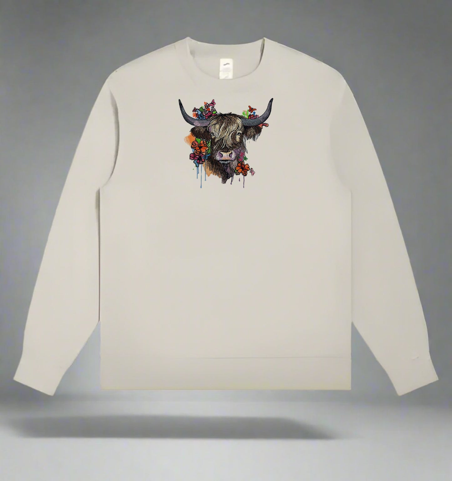Beige long-sleeve sweatshirt with a colorful cow design on a gray background