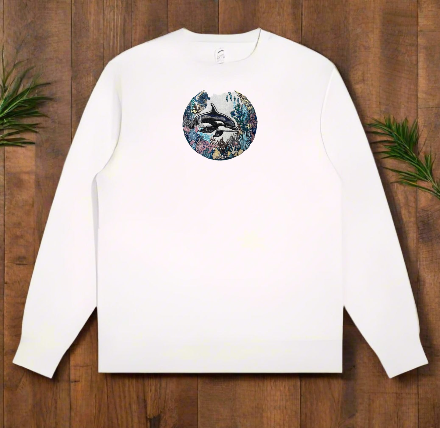 White long-sleeve sweatshirt with a circular design featuring a dolphin on a wooden surface.