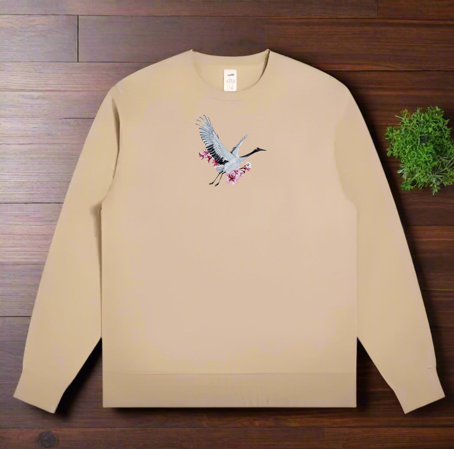 khaki sweatshirt with a Sakura Crane Embroidery – Elegant Serenity design on a wooden surface