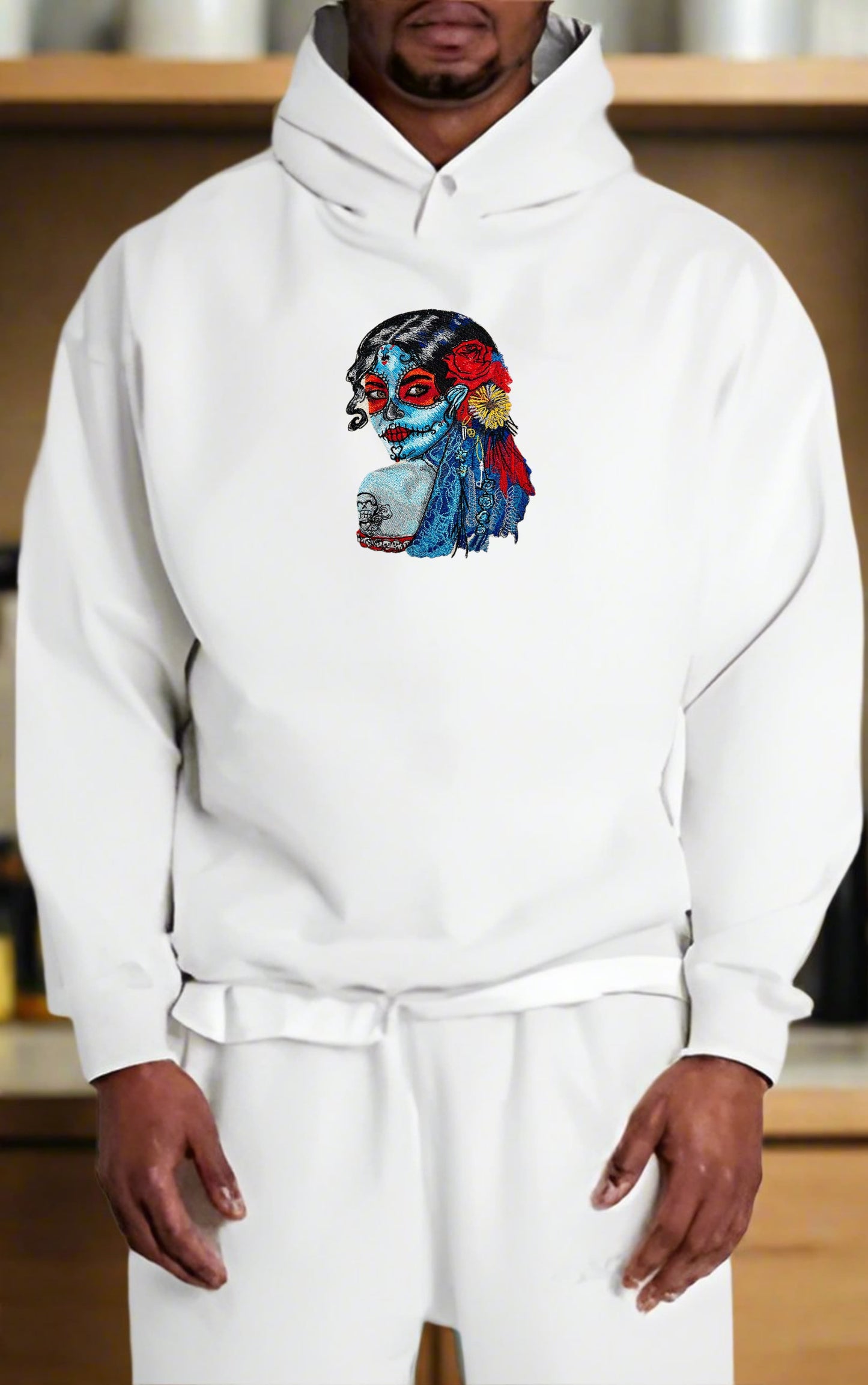 Person wearing a white hoodie with a colorful Sugar Skull Lady Embroidery – Día de los Muertos Art design on a wooden shelf background