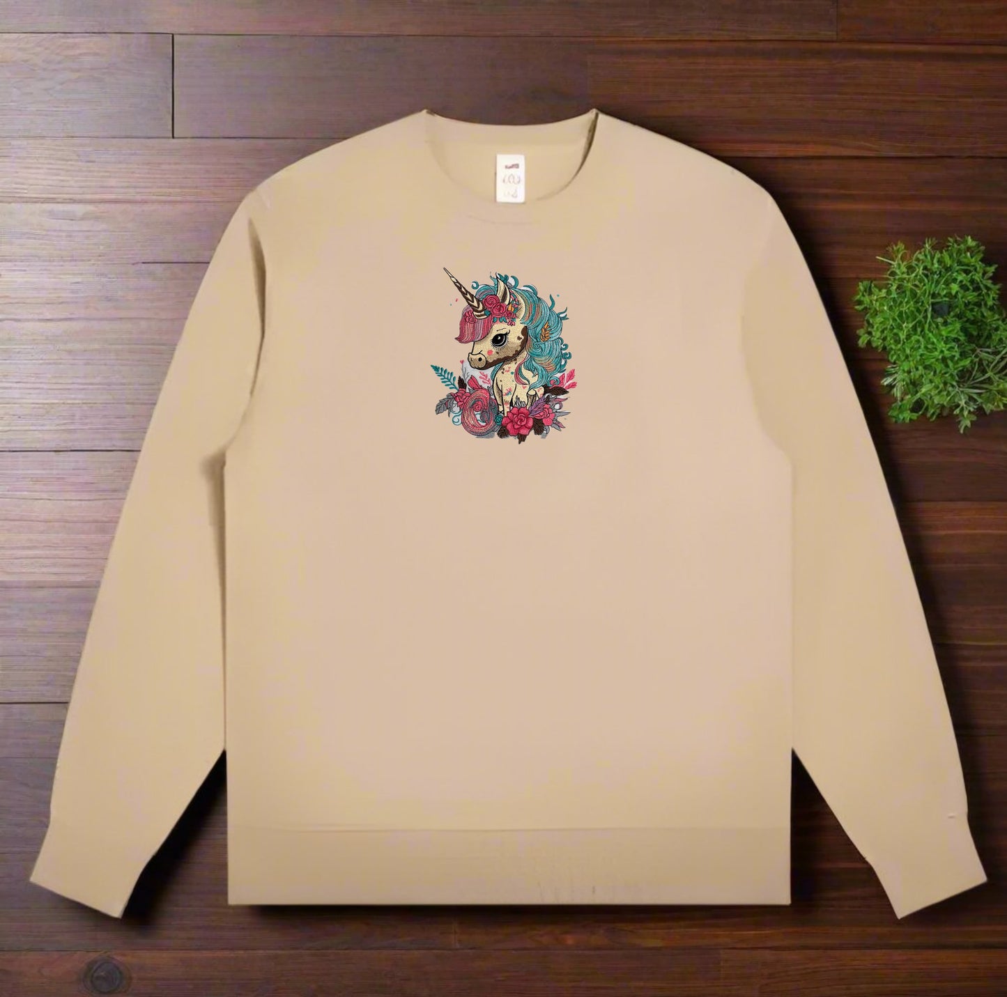 Beige sweatshirt with a colorful unicorn design on a wooden surface