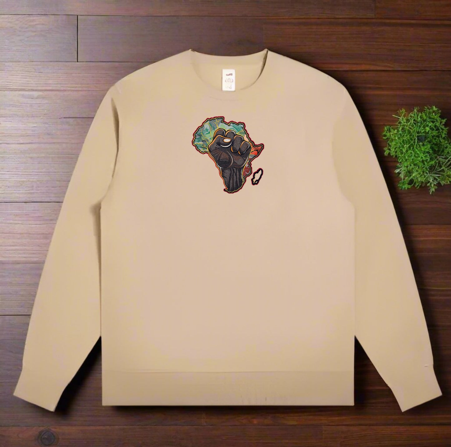 Beige sweatshirt with a African Unity Fist Embroidery – Empowerment design on a wooden surface