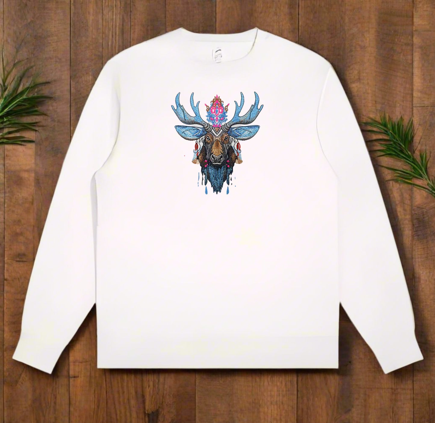 A colorful embroidery design of a moose with blue and brown colors, featuring intricate details and decorative elements on white sweatshirt