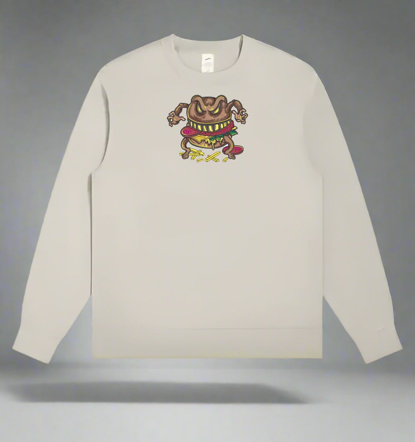 Beige long-sleeve sweatshirt with a Cursed Burger Monster Embroidery – Funky Foodie of a creature on a gray background