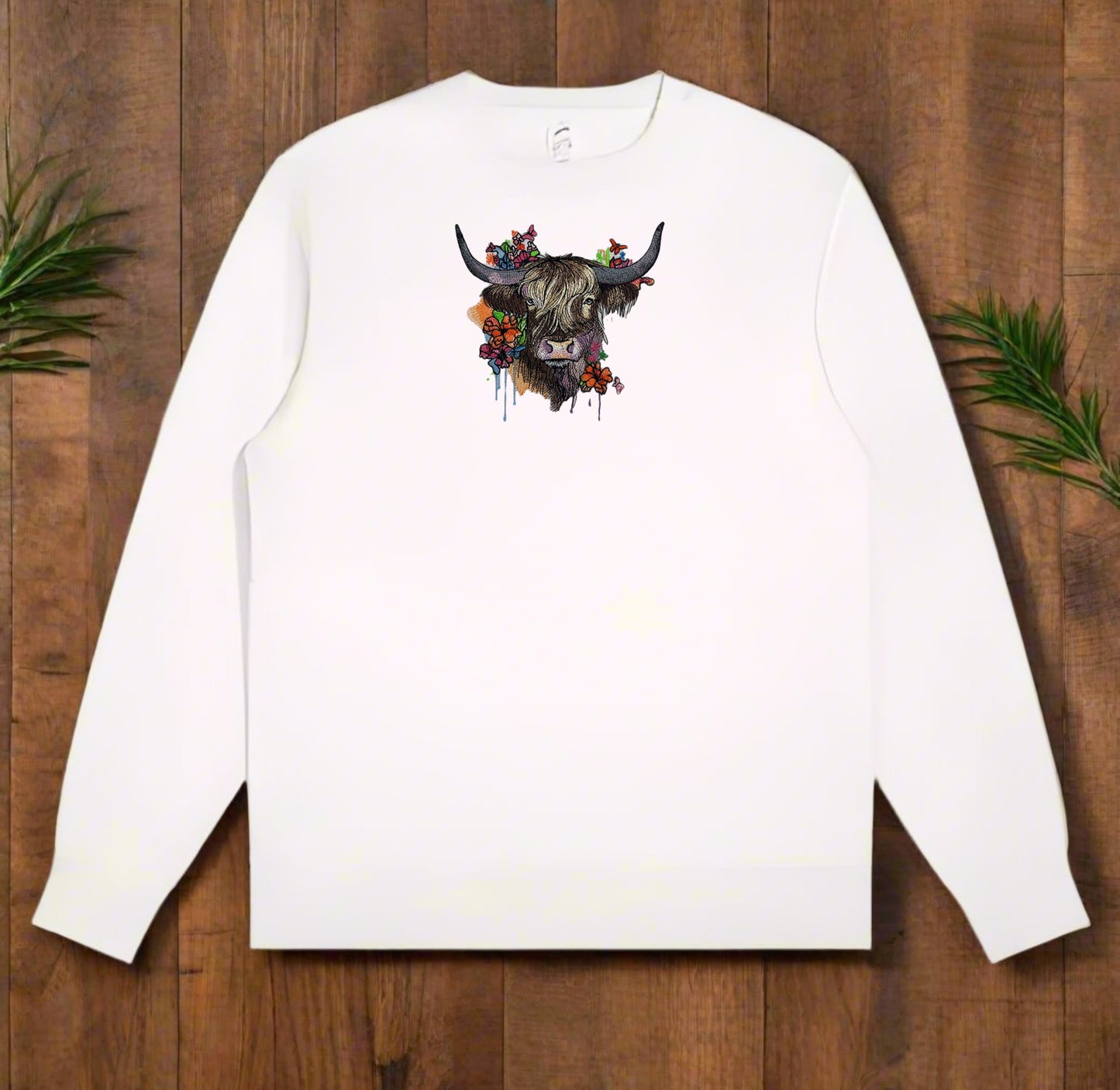 White long-sleeve sweatshirt with a decorative yak design on a wooden surface.