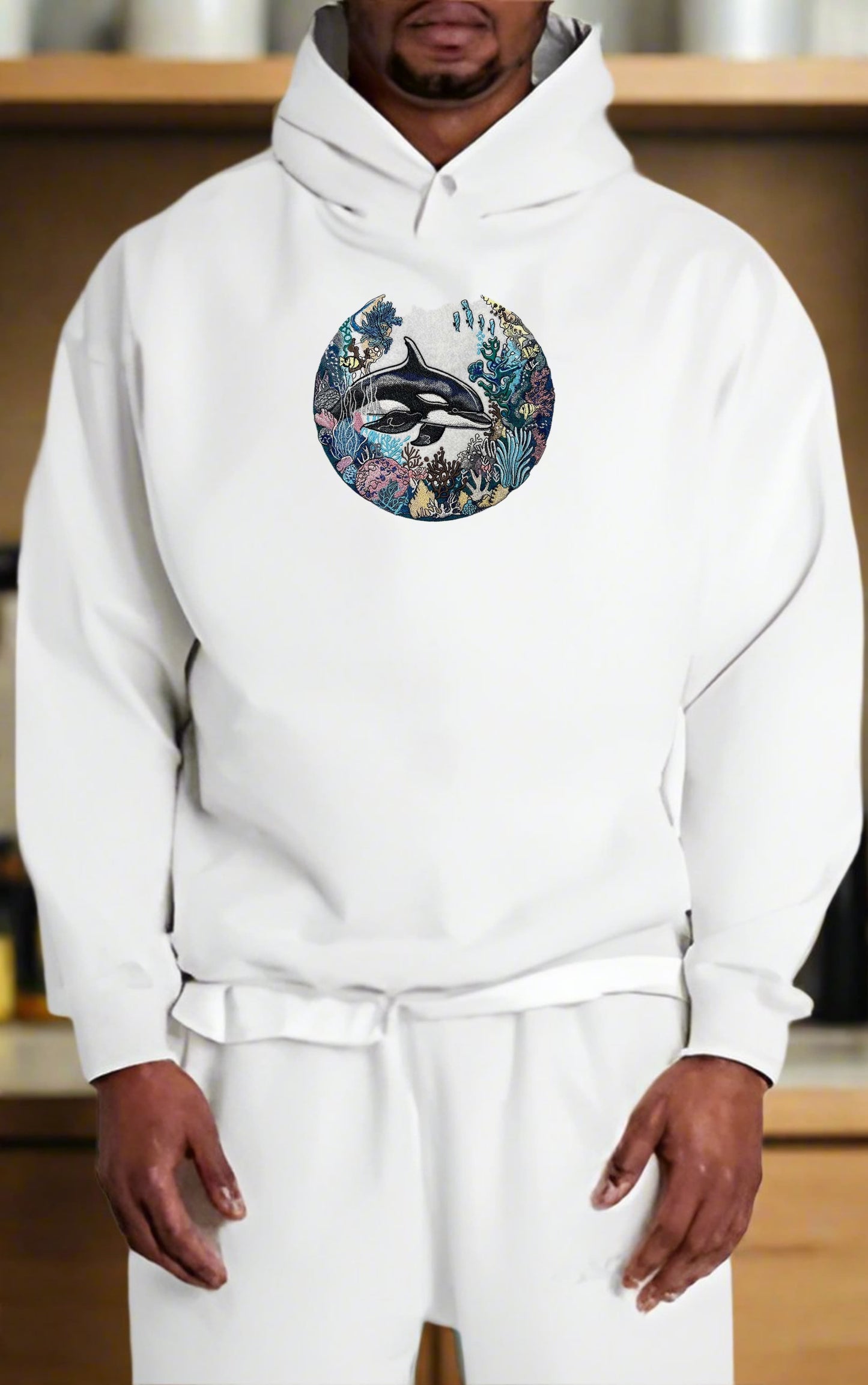 Person wearing a white hoodie with a colorful orca design on a wooden shelf background
