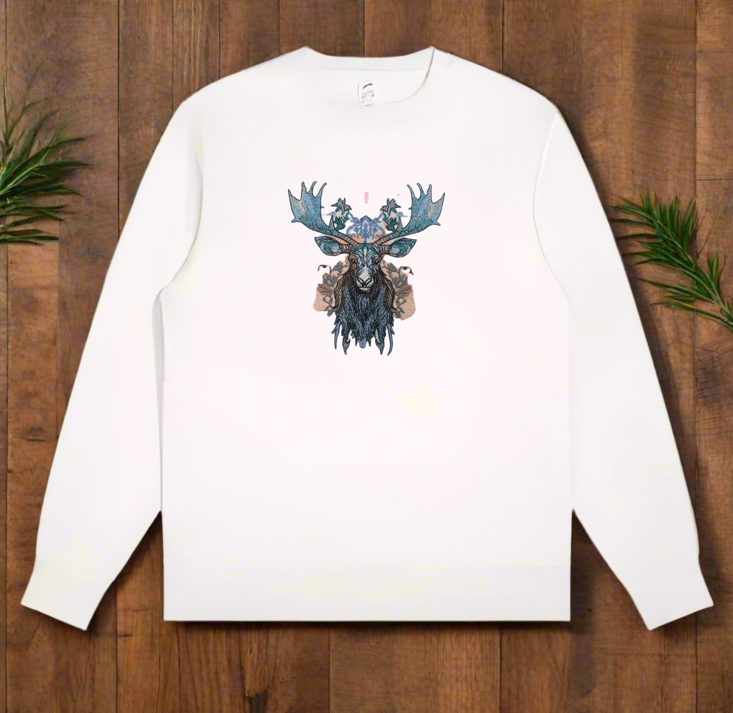 A stitched embroidery design of a moose head with ornate antlers and a floral pattern in blue, gray, and pink colors on a white sweatshirt background.