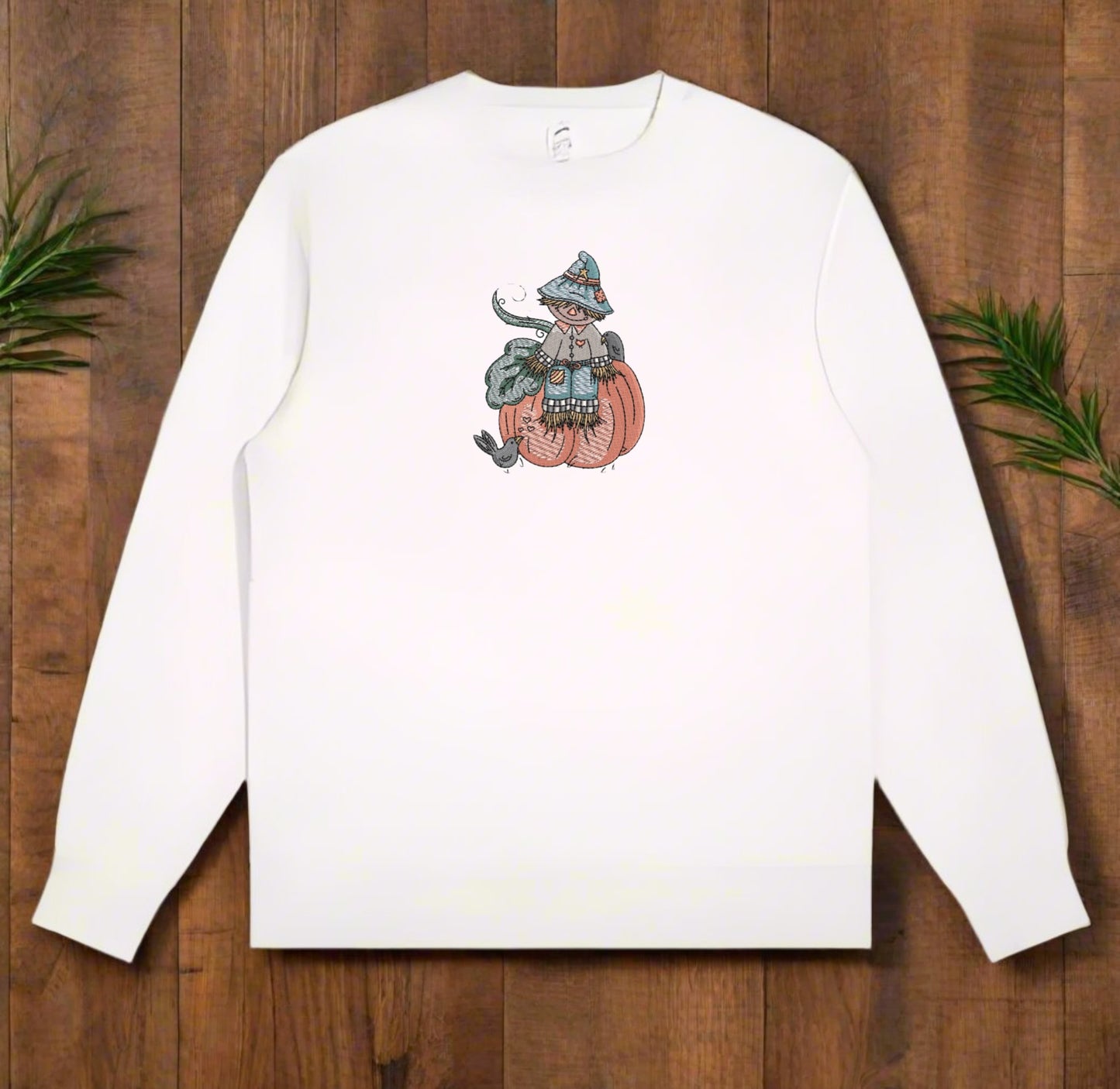 White long-sleeve shirt with a graphic design of a person on a pumpkin on a wooden surface.