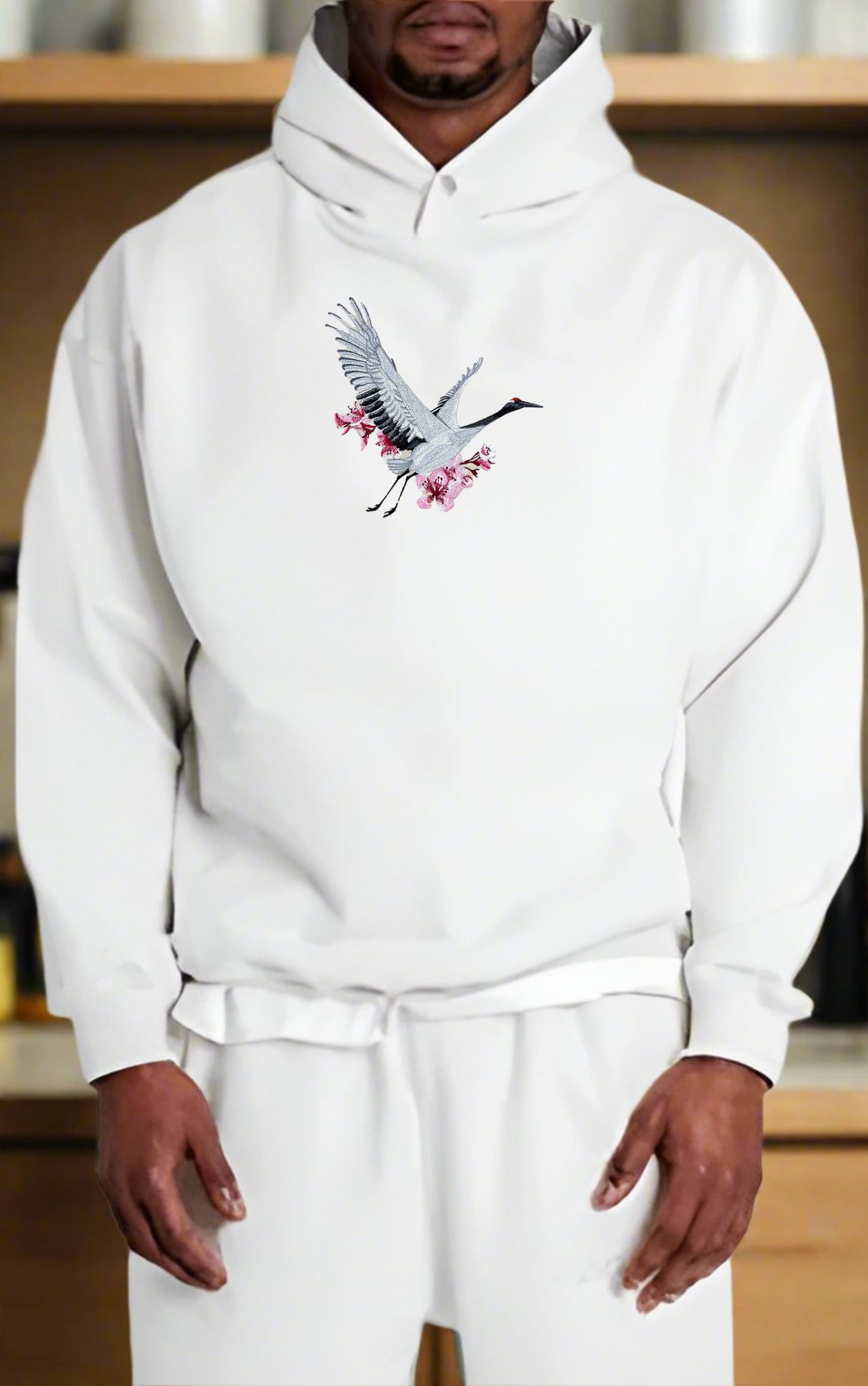 Person wearing a white hoodie with a crane design in a room.