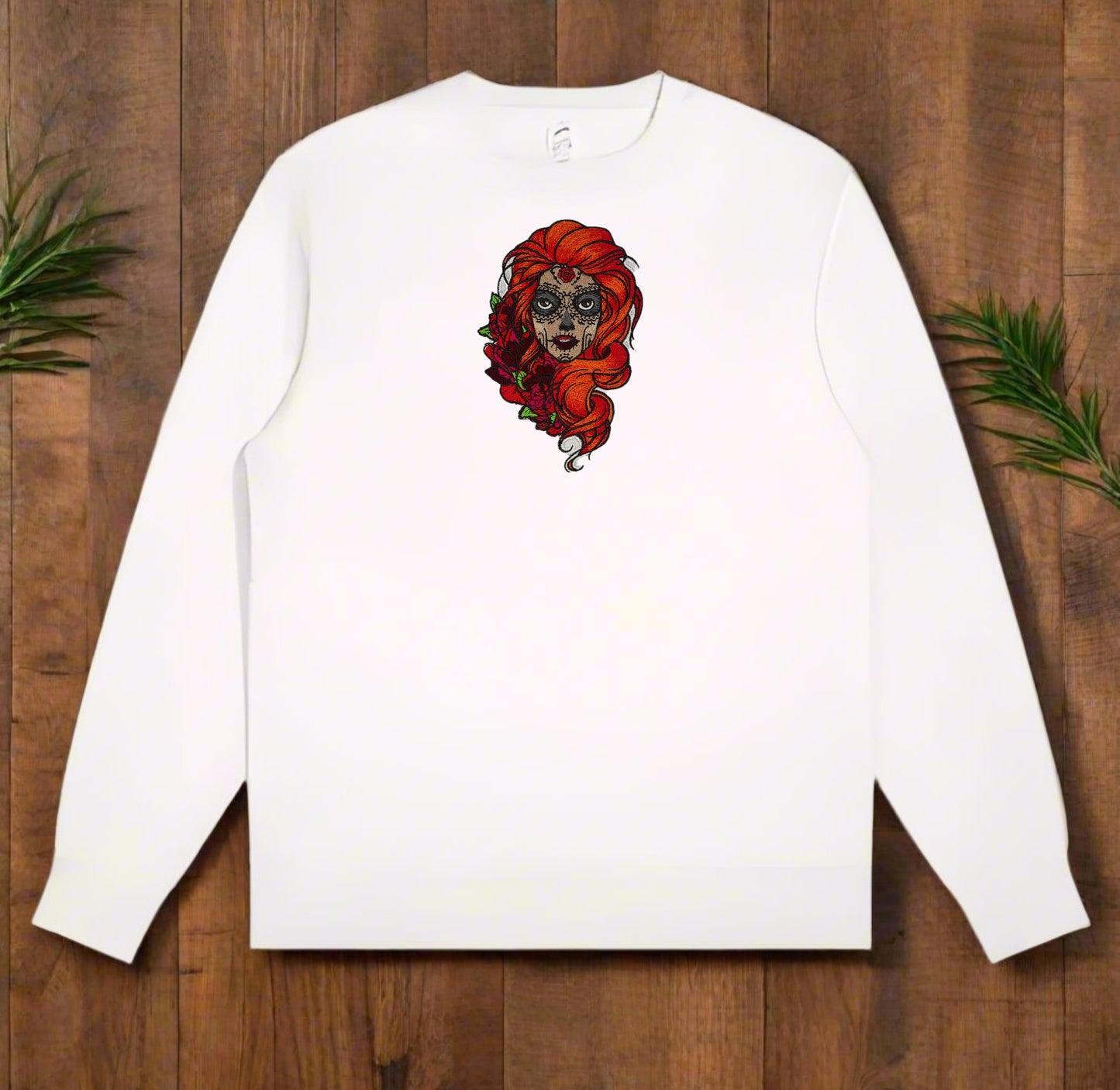 White long-sleeve shirt with a Sugar Skull Rose Embroidery – Artistic Heritage design on a wooden surface