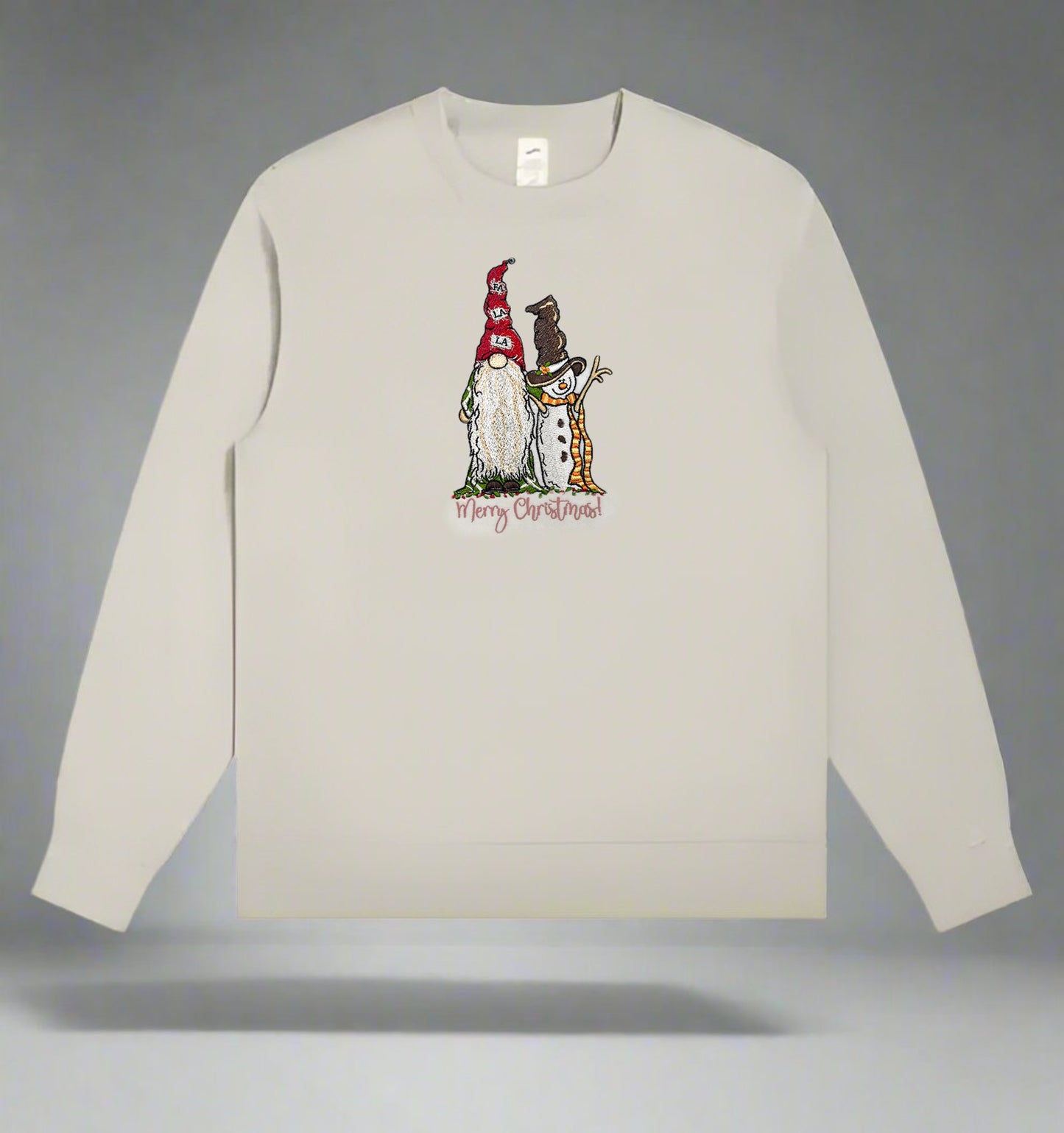 Light beige crewneck sweatshirt featuring an embroidered gnome and snowman with the phrase “Merry Christmas!” centered on the chest.