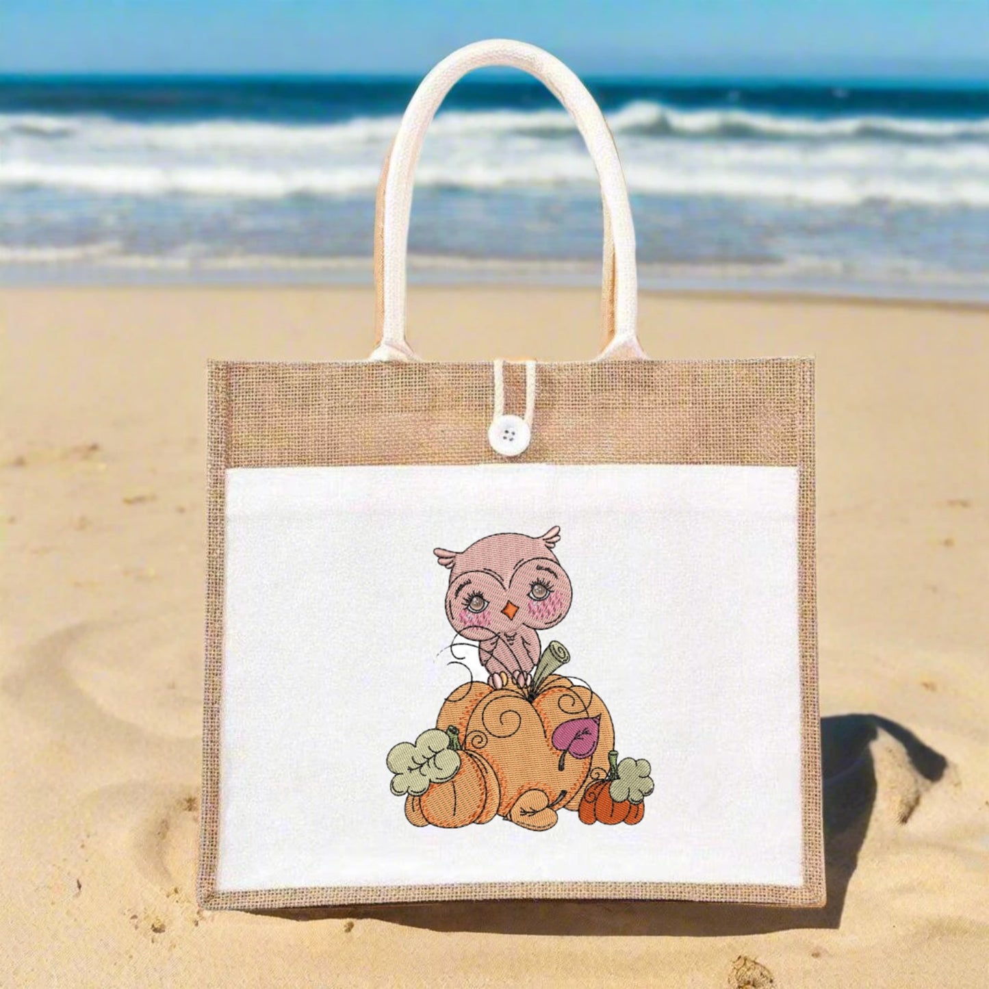 Jute bag with an owl design on a sandy beach with ocean in the background