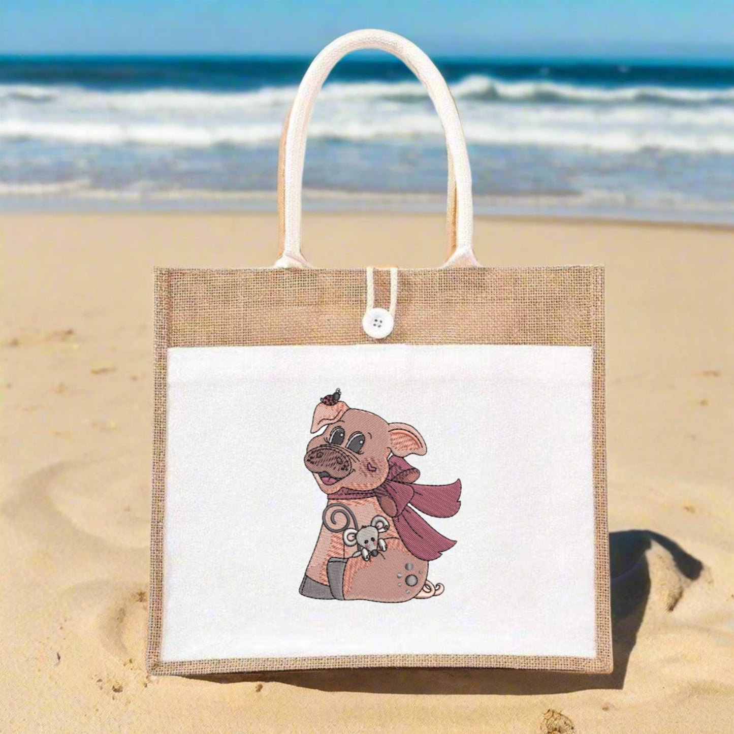 Jute bag with a cartoon pig design on a sandy beach with ocean in the background