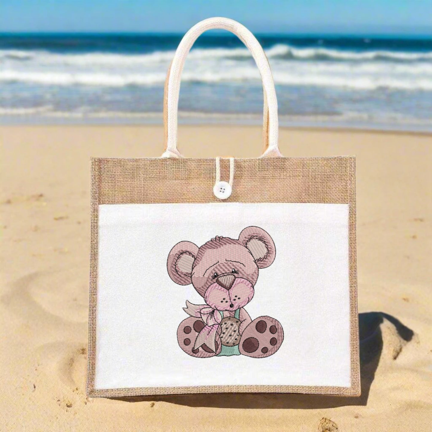 Jute bag with a teddy bear design on a sandy beach with ocean in the background