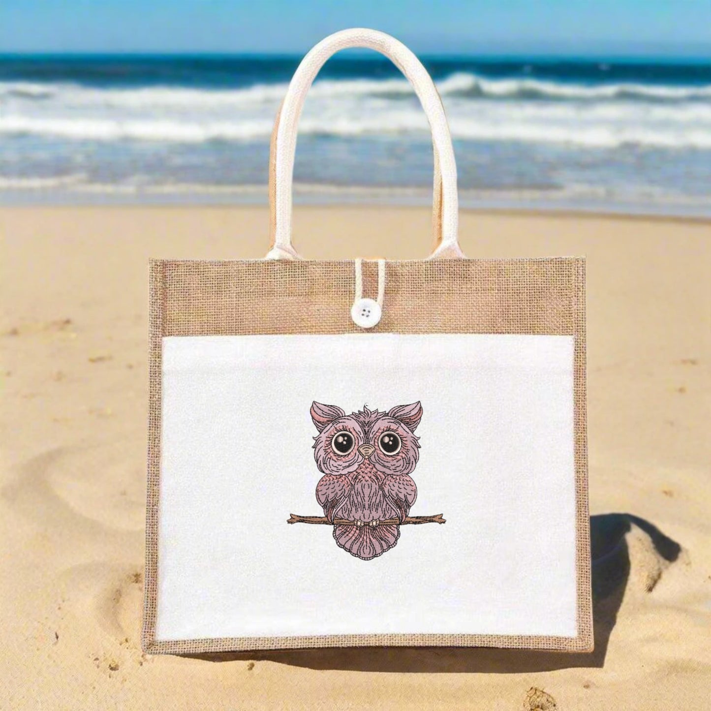 Jute bag with an owl design on a sandy beach with ocean in the background