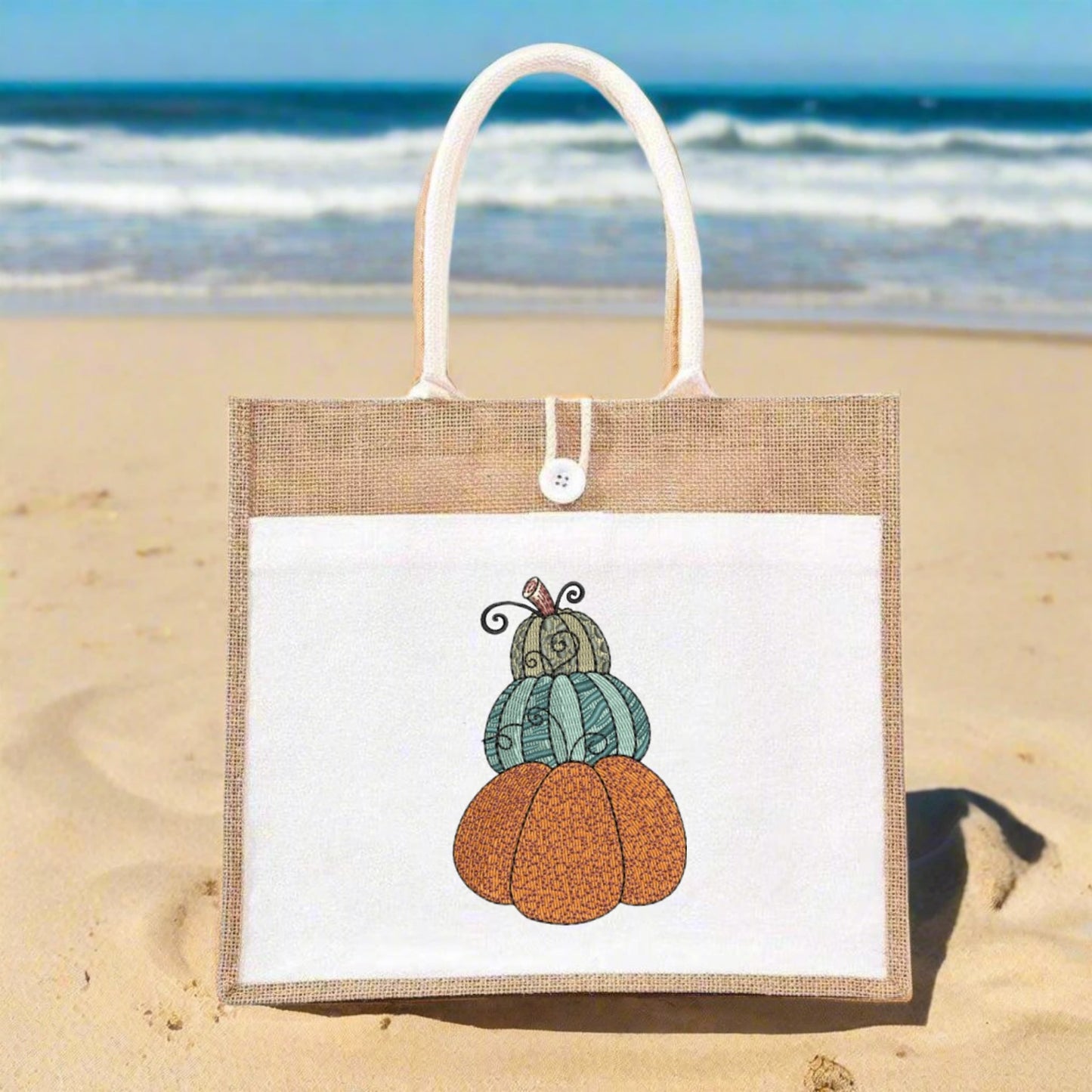 Tote bag with pumpkin design on a sandy beach with ocean in the background