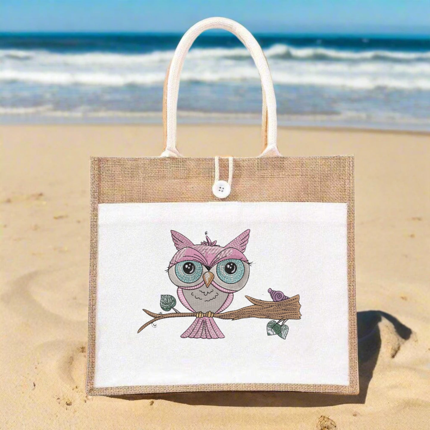 Jute bag with an owl design on a sandy beach with ocean in the background