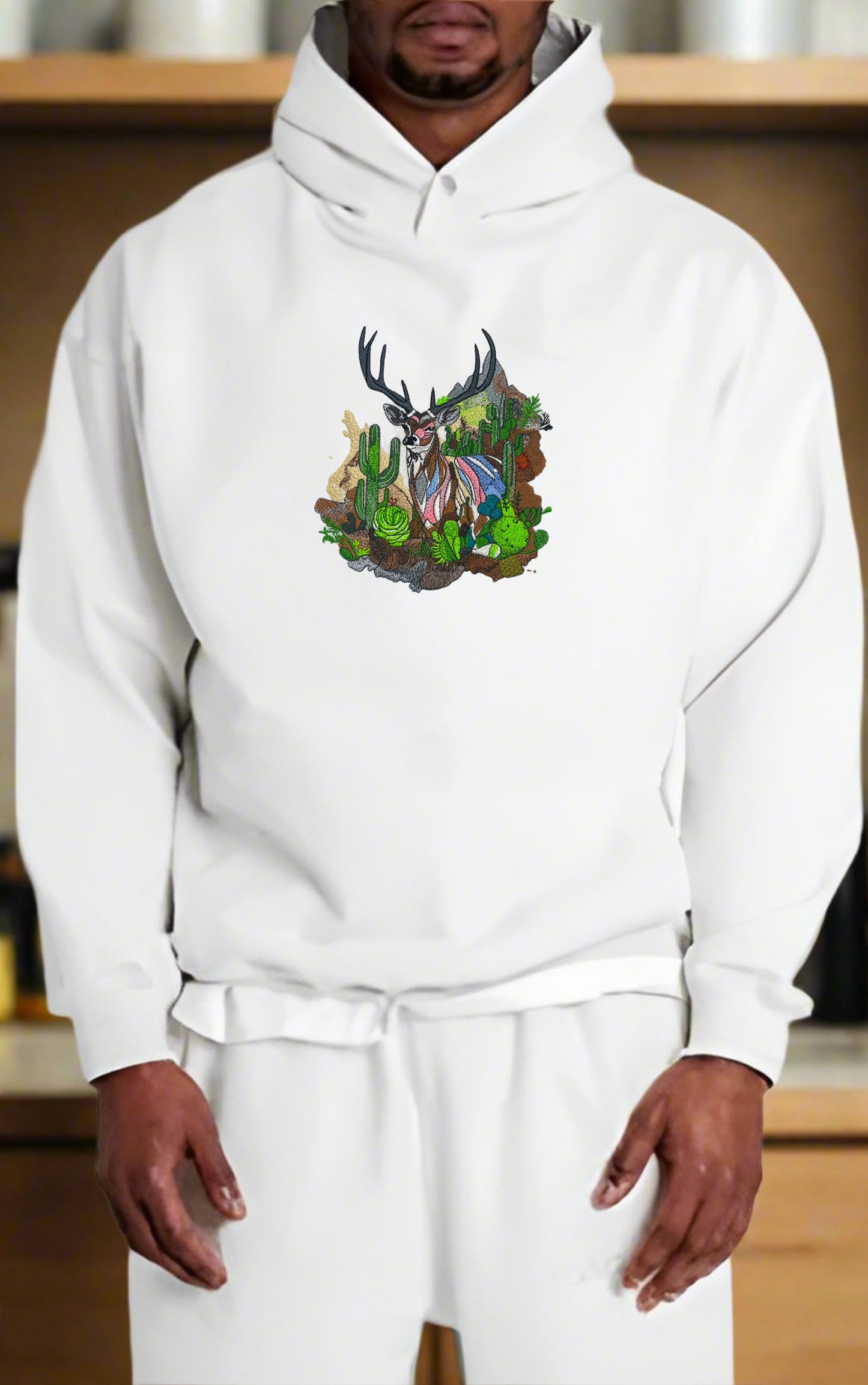 Embroidered hoodie featuring a mountain deer with Ombre antlers, surrounded by wildflowers and alpine pines, in a colorful design.