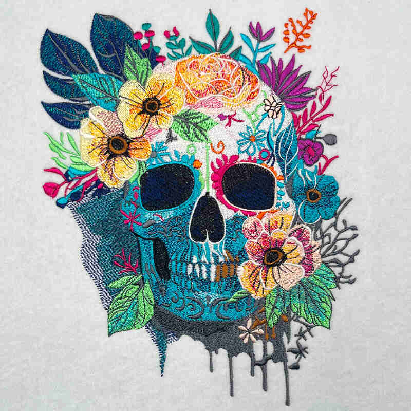Embroidered design featuring a skull surrounded by a variety of colorful flowers, designed in a floral and gothic style.