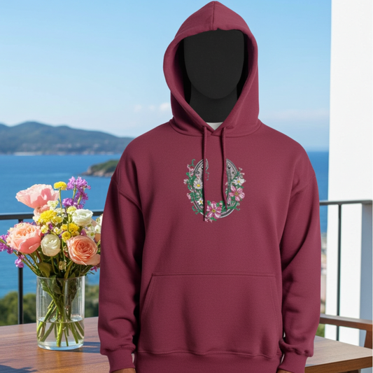 Burgundy hoodie mockup featuring a floral embroidered horseshoe design on the chest, photographed on a balcony with ocean view and a vase of colorful flowers.