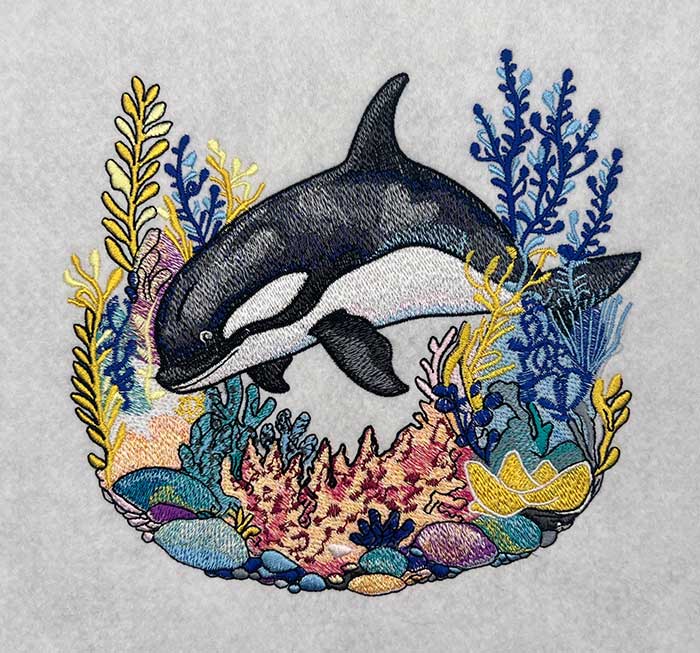 Embroidered design featuring a majestic orca whale surrounded by colorful marine life and waves.