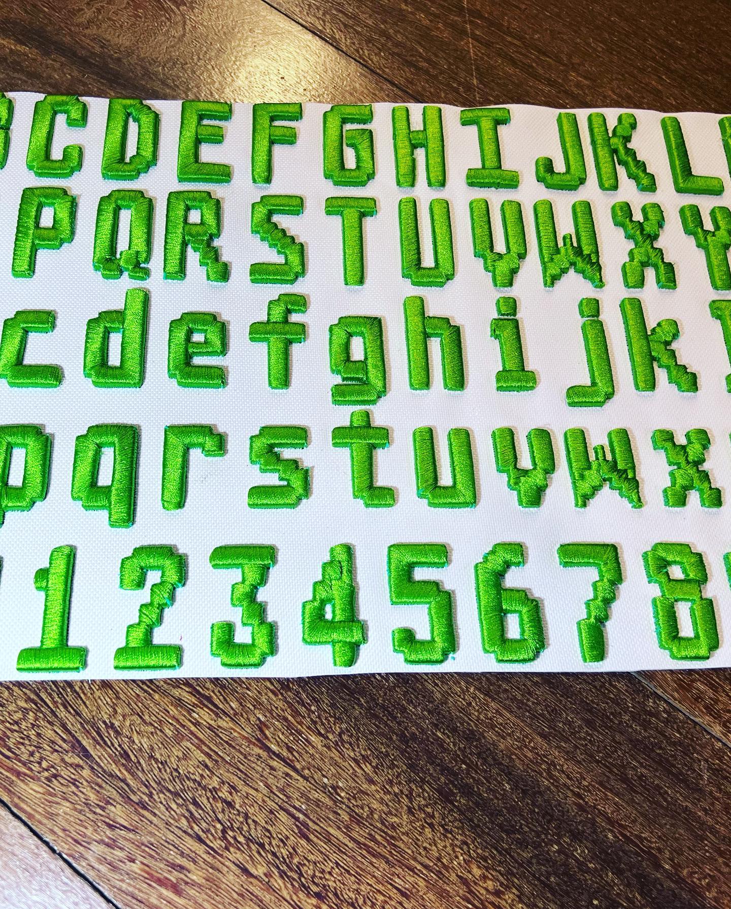 Sheet of green embroidered letters and numbers on a wooden surface