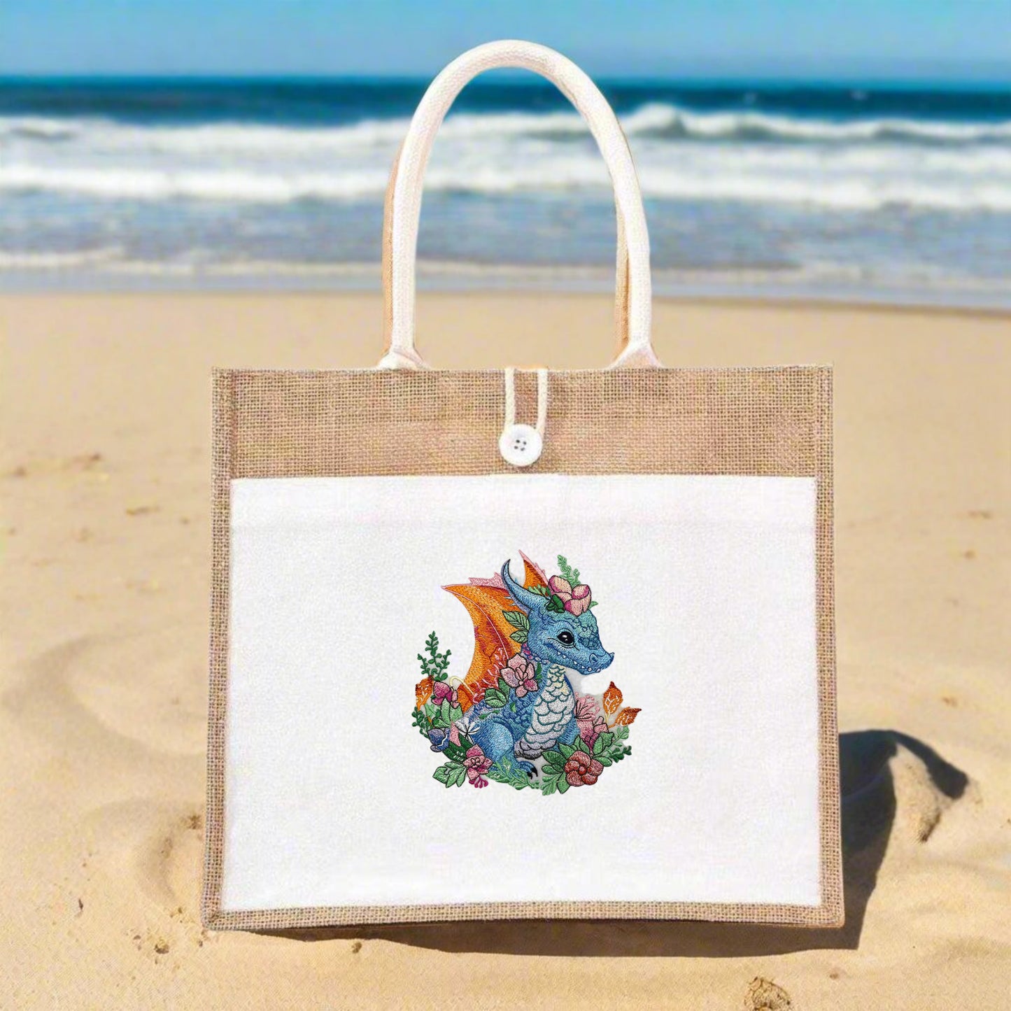 A hand-stitched embroidered jute tote featuring a vibrant blue dragon with orange wings, surrounded by green foliage and pink flowers.