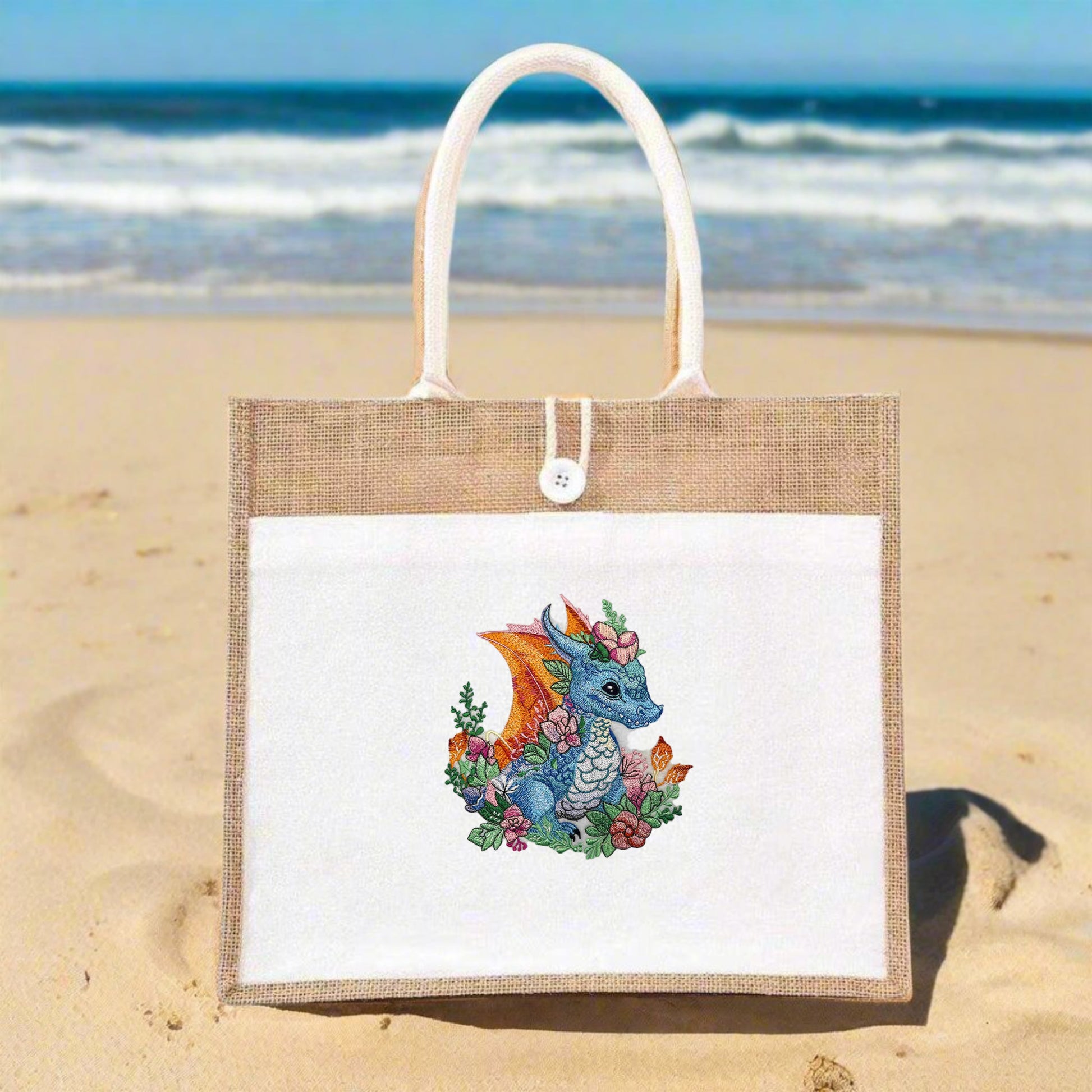 A hand-stitched embroidered jute tote featuring a vibrant blue dragon with orange wings, surrounded by green foliage and pink flowers.