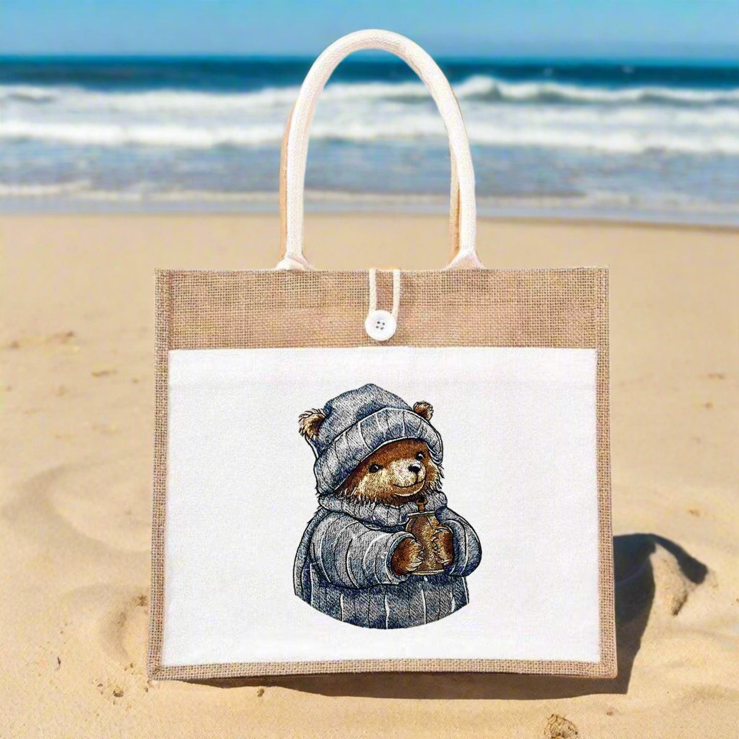 Embroidered image of a frosty bear wearing a hat and coat, holding a mug, on a jute tote bag.