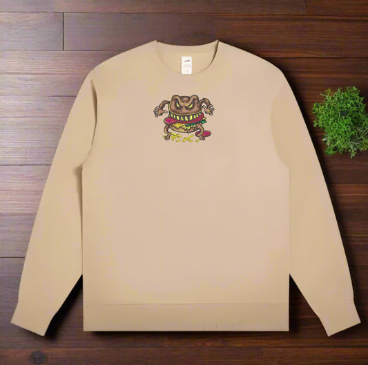Beige sweatshirt with a  Cursed Burger Monster Embroidery – Funky Foodie design on a wooden surface