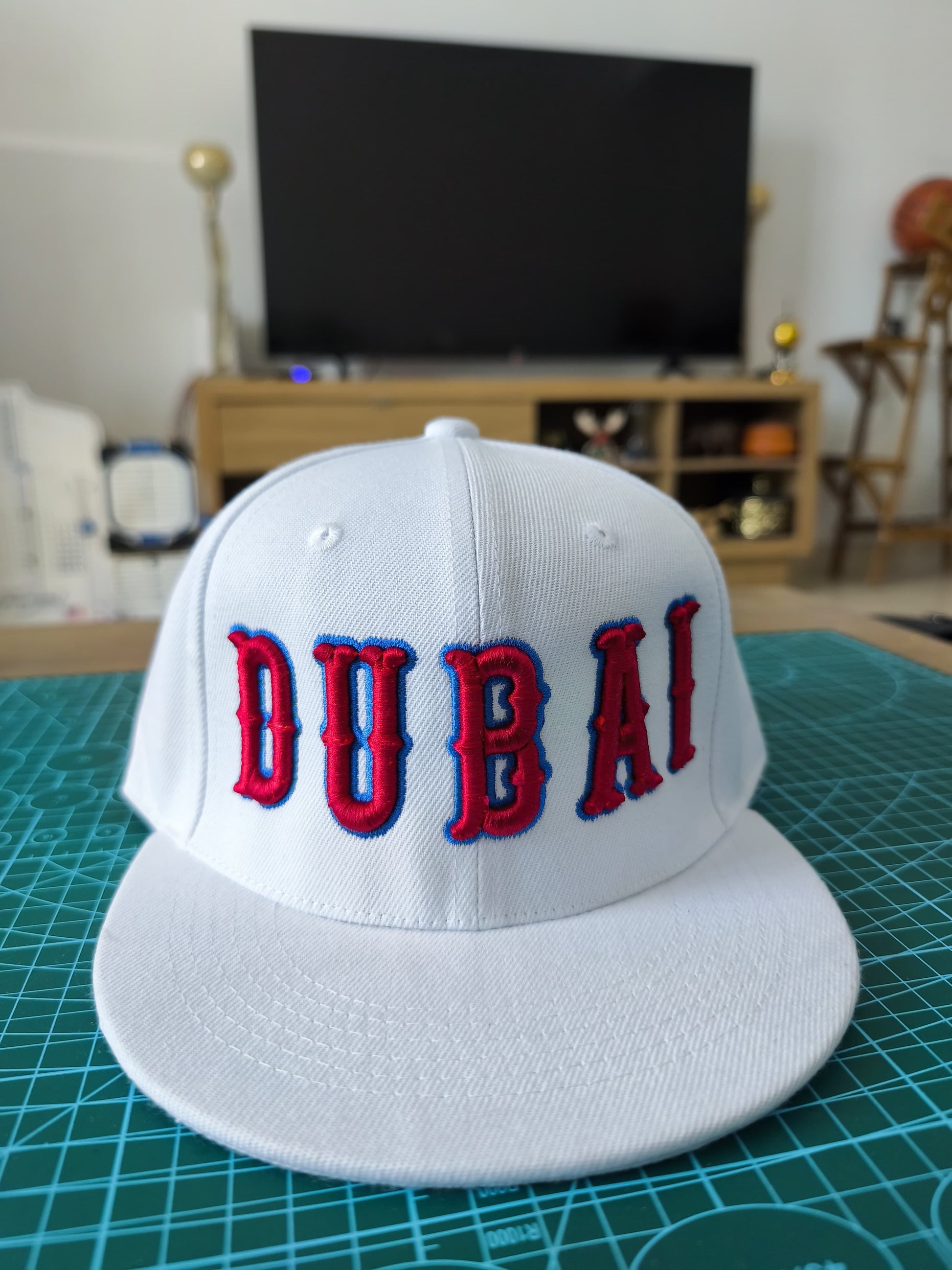 White cap with 'DUBAI' in red and blue on a green cutting mat.
