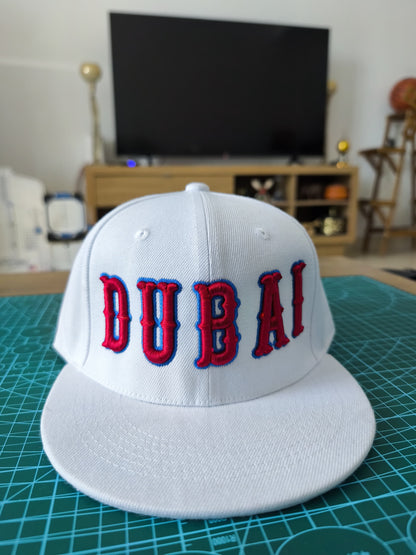 White cap with 'DUBAI' in red and blue on a green cutting mat.