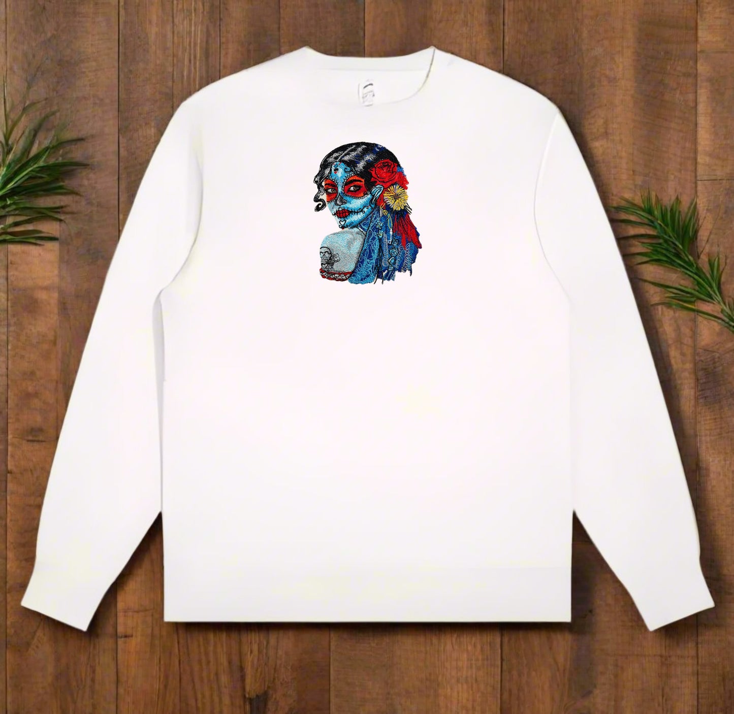 White long-sleeve sweatshirt with a colorful  Daydream Muse Sugar Skull Embroidery on a wooden surface