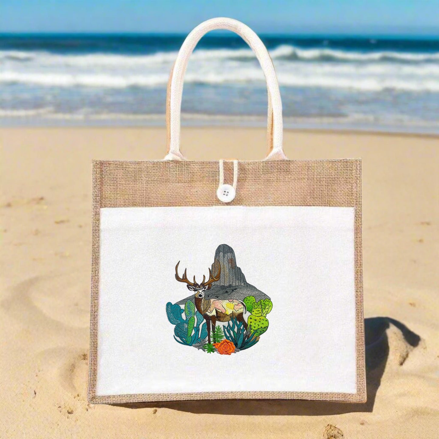 A jute tote bag with intricate embroidery of a mountain buck among floral and mountainous terrain.