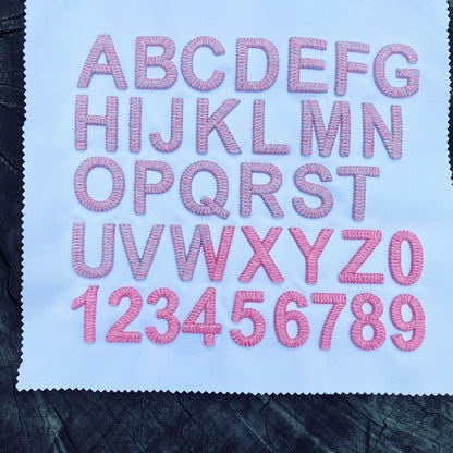 Embroidered letters and numbers on a fabric swatch with pink thread.
