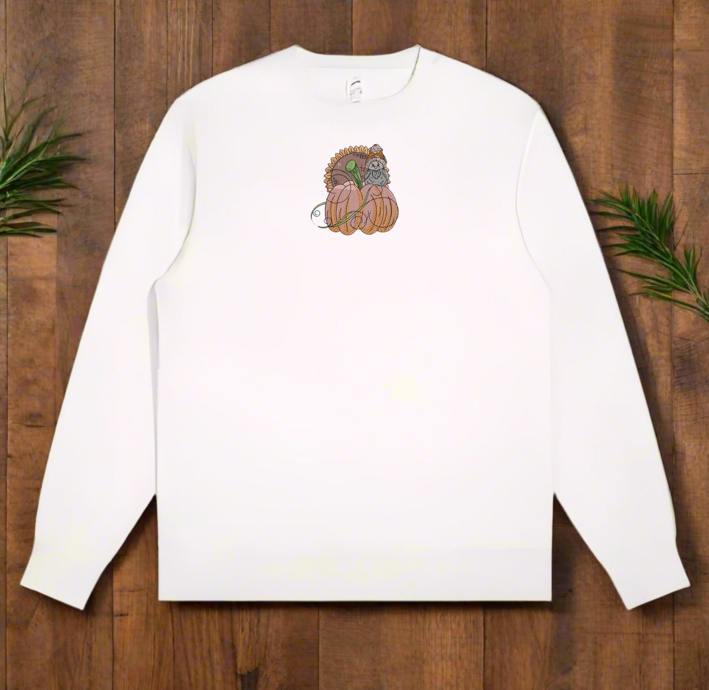 White long-sleeve sweatshirt with a Pumpkin Bird & Sunflower Embroidery Design on a wooden surface