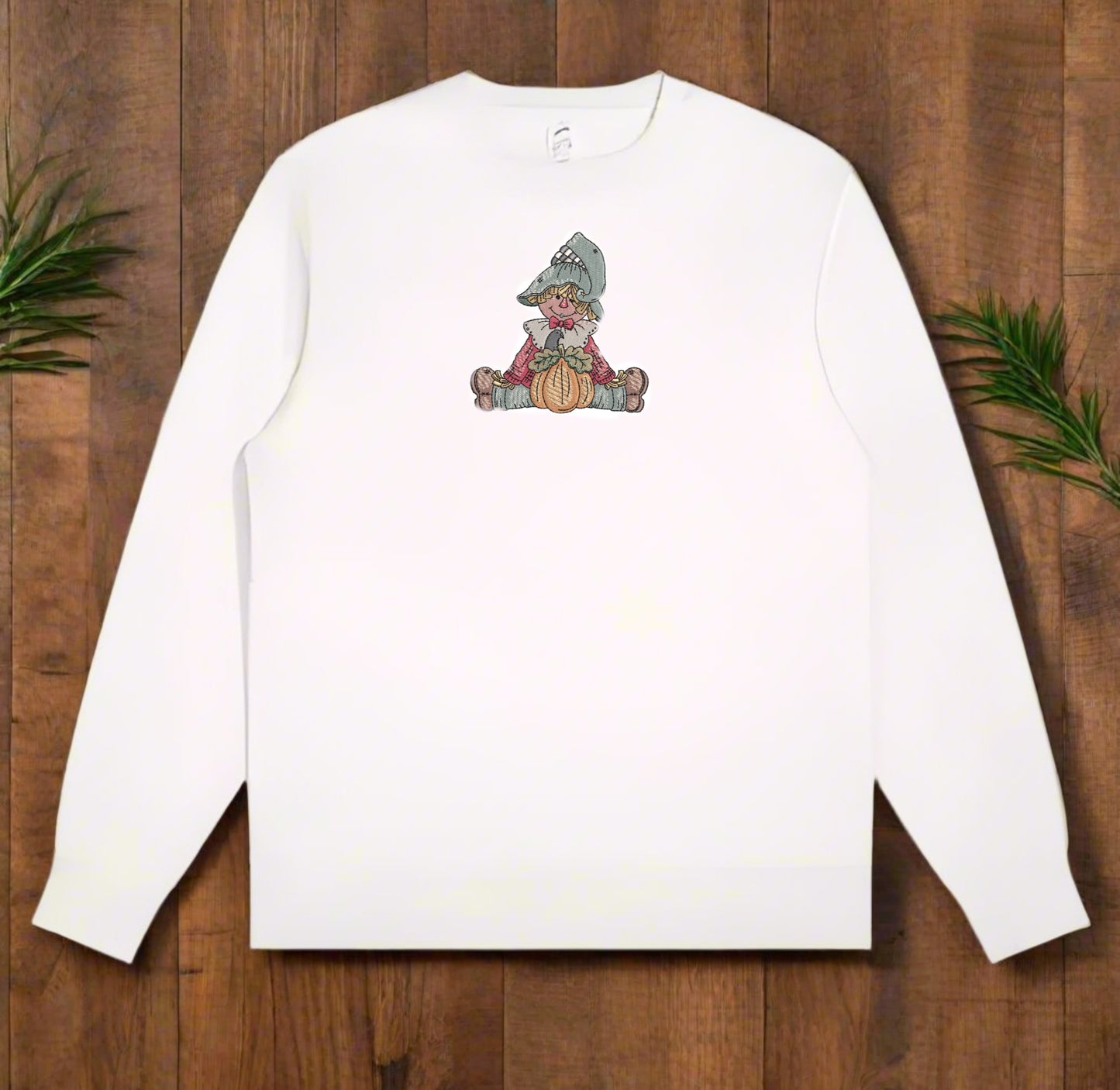 White long-sleeve sweatshirt with a embroidered design on a wooden surface