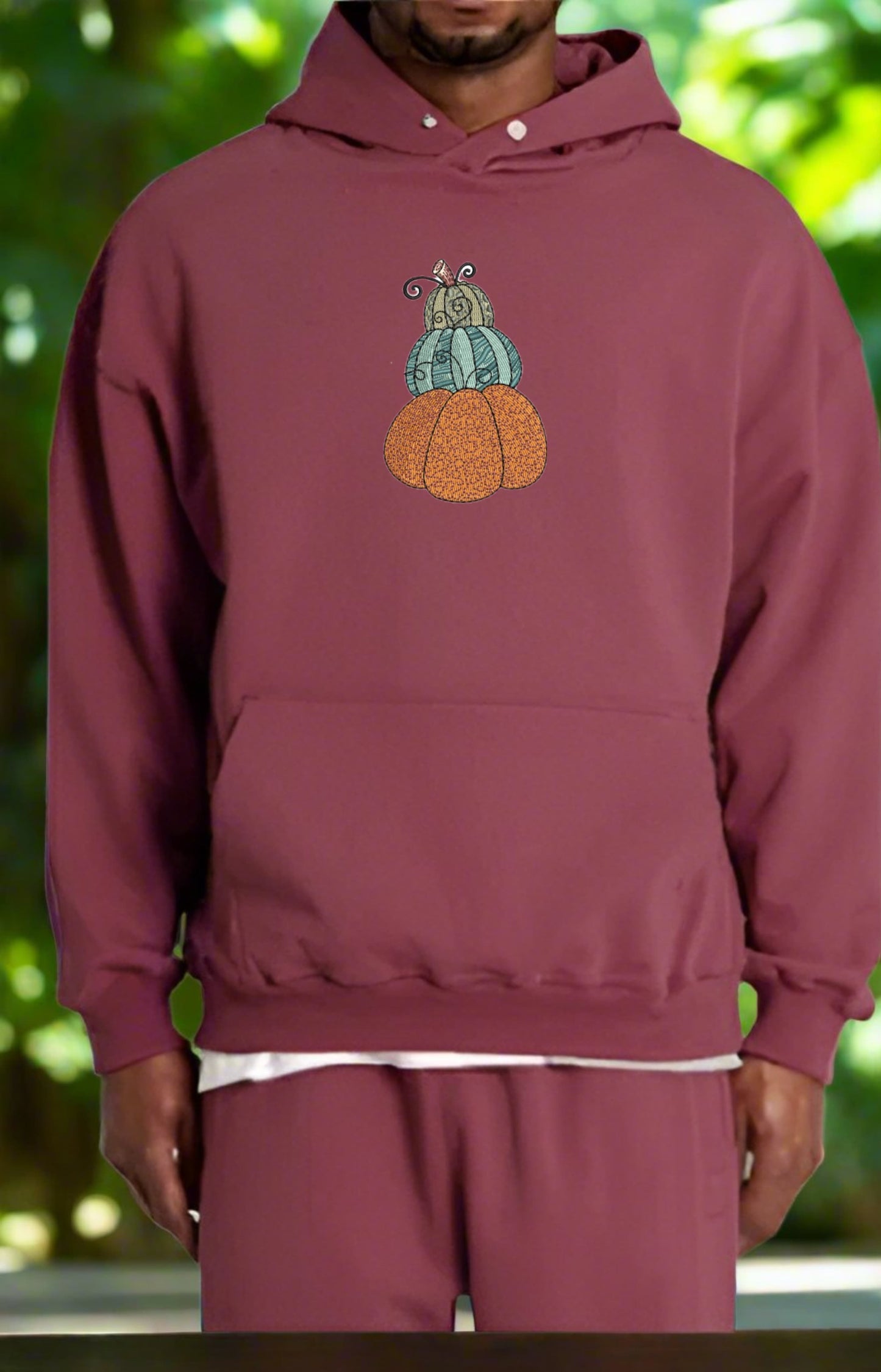 Person wearing a maroon hoodie with a colorful pumpkin design against a blurred green background