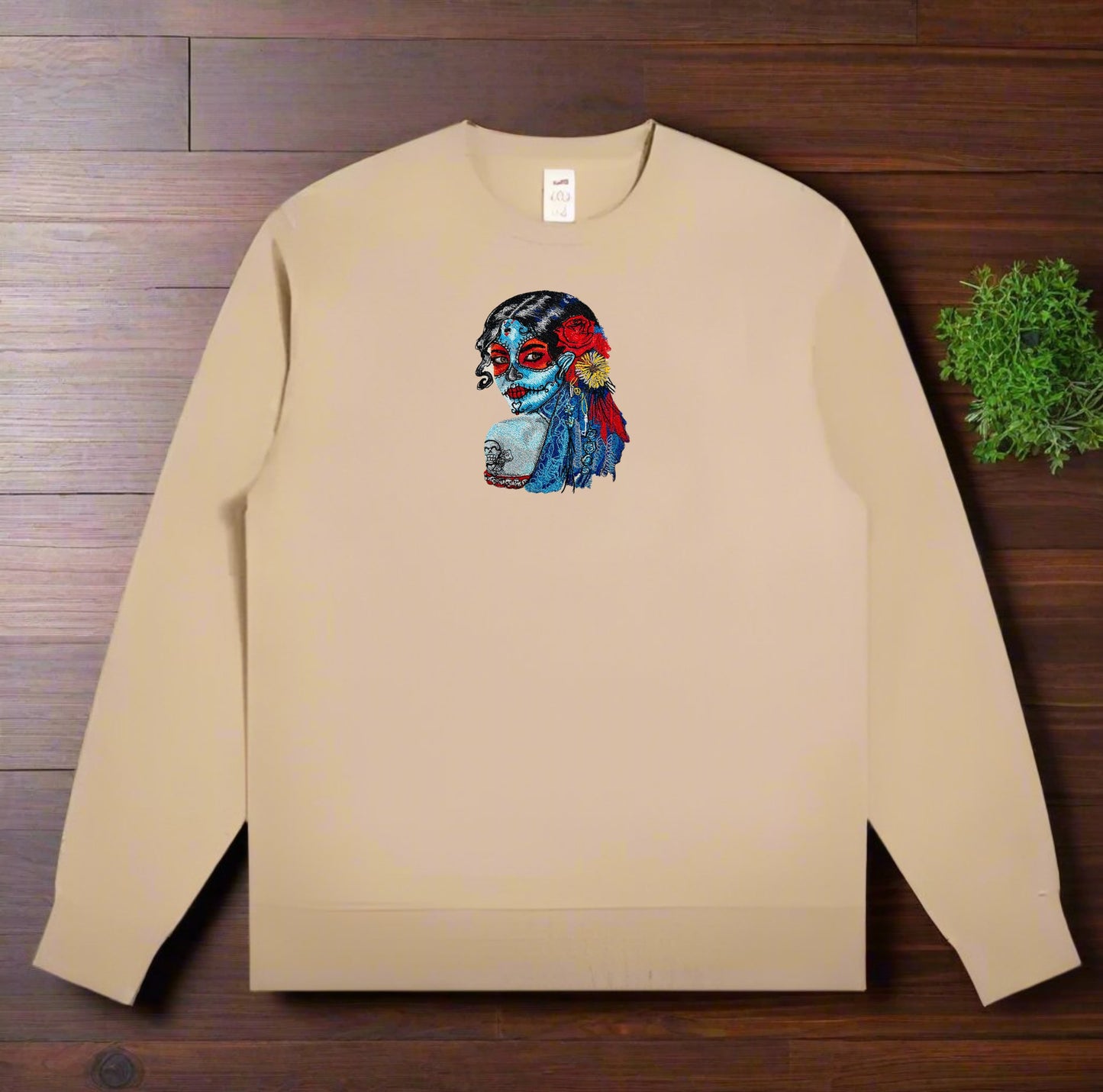 Beige sweatshirt with a colorful Daydream Muse Sugar Skull Embroidery design on a wooden surface
